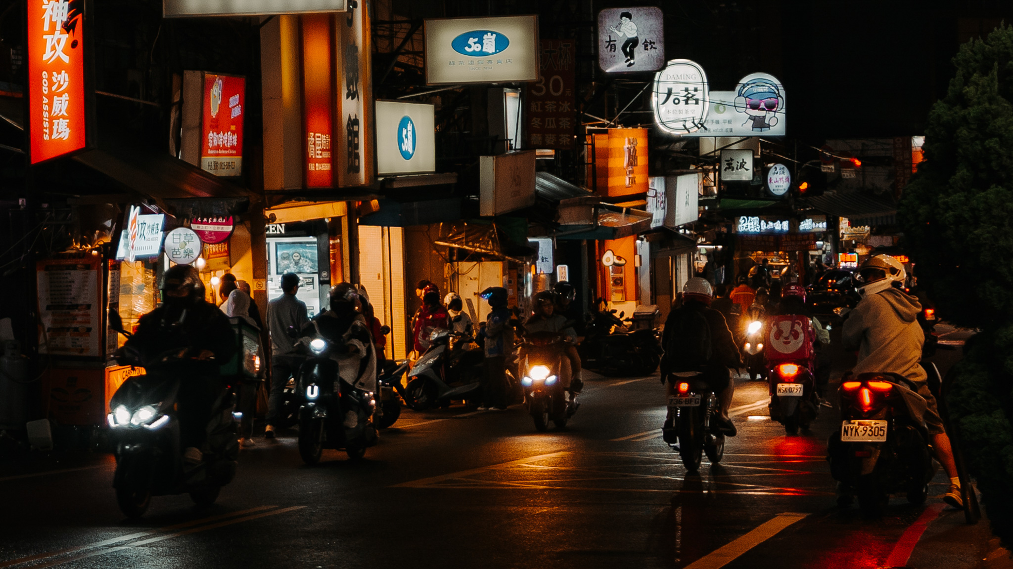 Busy Taiwan night market road with scooters and illuminated signs